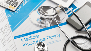 Image of a tabletop cluttered with a stethoscope, phone, and document with a header stating, "Medical Insurance Policy."